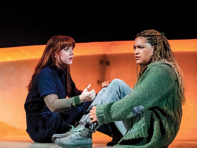 Two actors seated on the floor in tense discussion