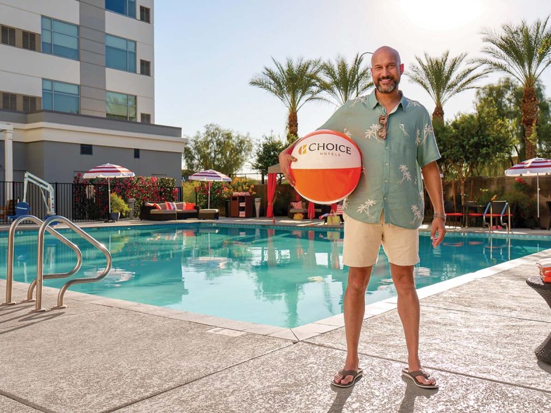 Keegan-Michael Key, a man in a hawaiian shirt, standing by a pool while holding a beach ball that says Choice Hotels