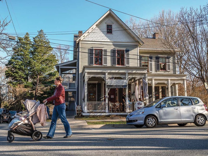 A woman and stroller walk past a large house-like building