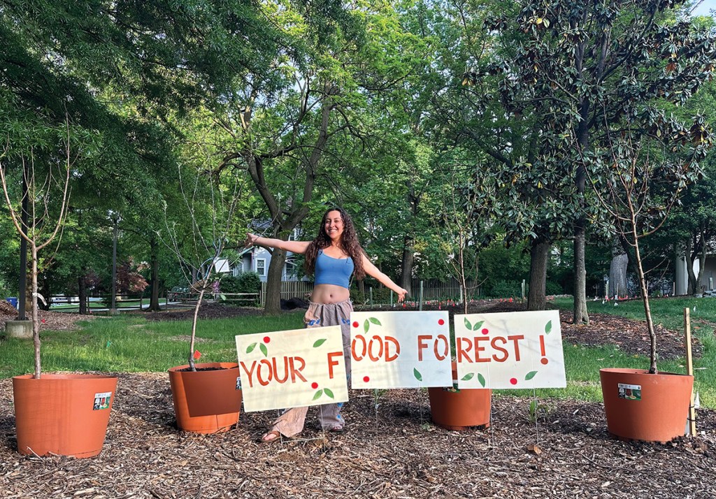 Tierney Acosta stands with signs that say "Your Food Forest!"