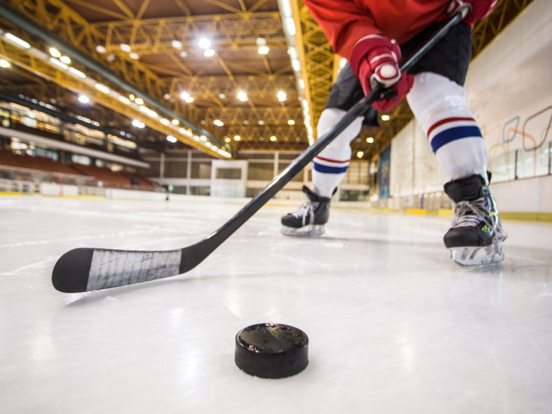 Unrecognizable ice hockey player at an ice hockey rink, holding a hockey stick.