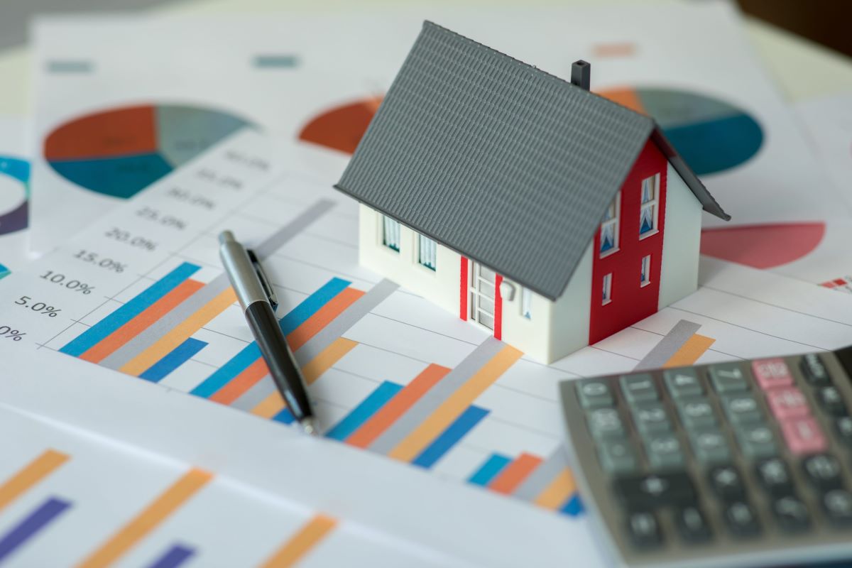 A model of a house, a pen, and a calculator are propped on top of stacks of paper graphs.