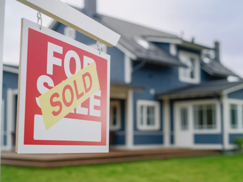 for sale sign covered with SOLD sign. House in the background