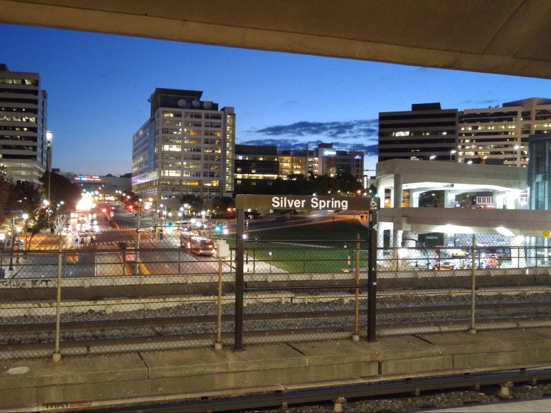 A Metro station sign reading "Silver Spring" with a city skyline in the background