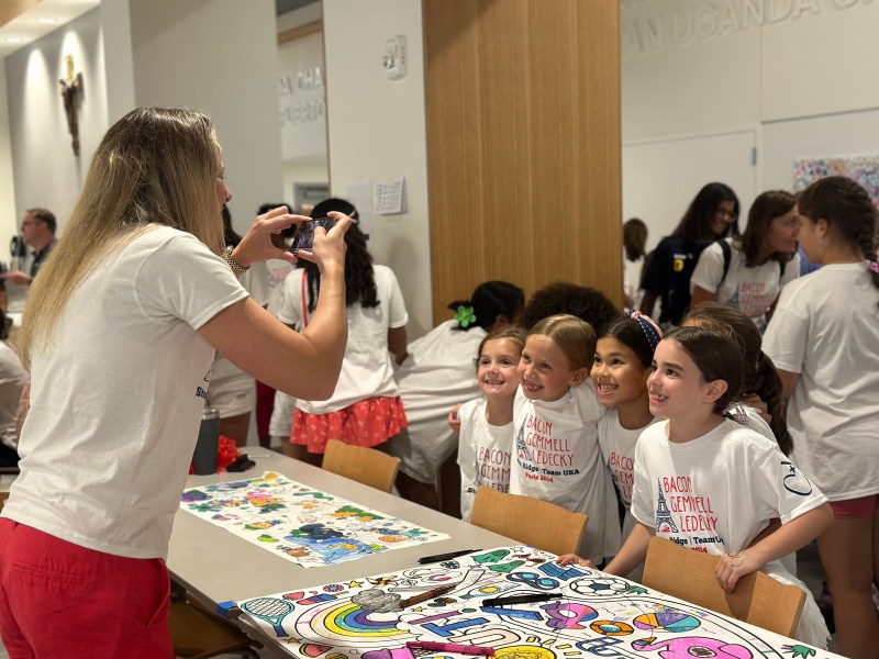 A woman takes a photo of a group of young girls posing together.