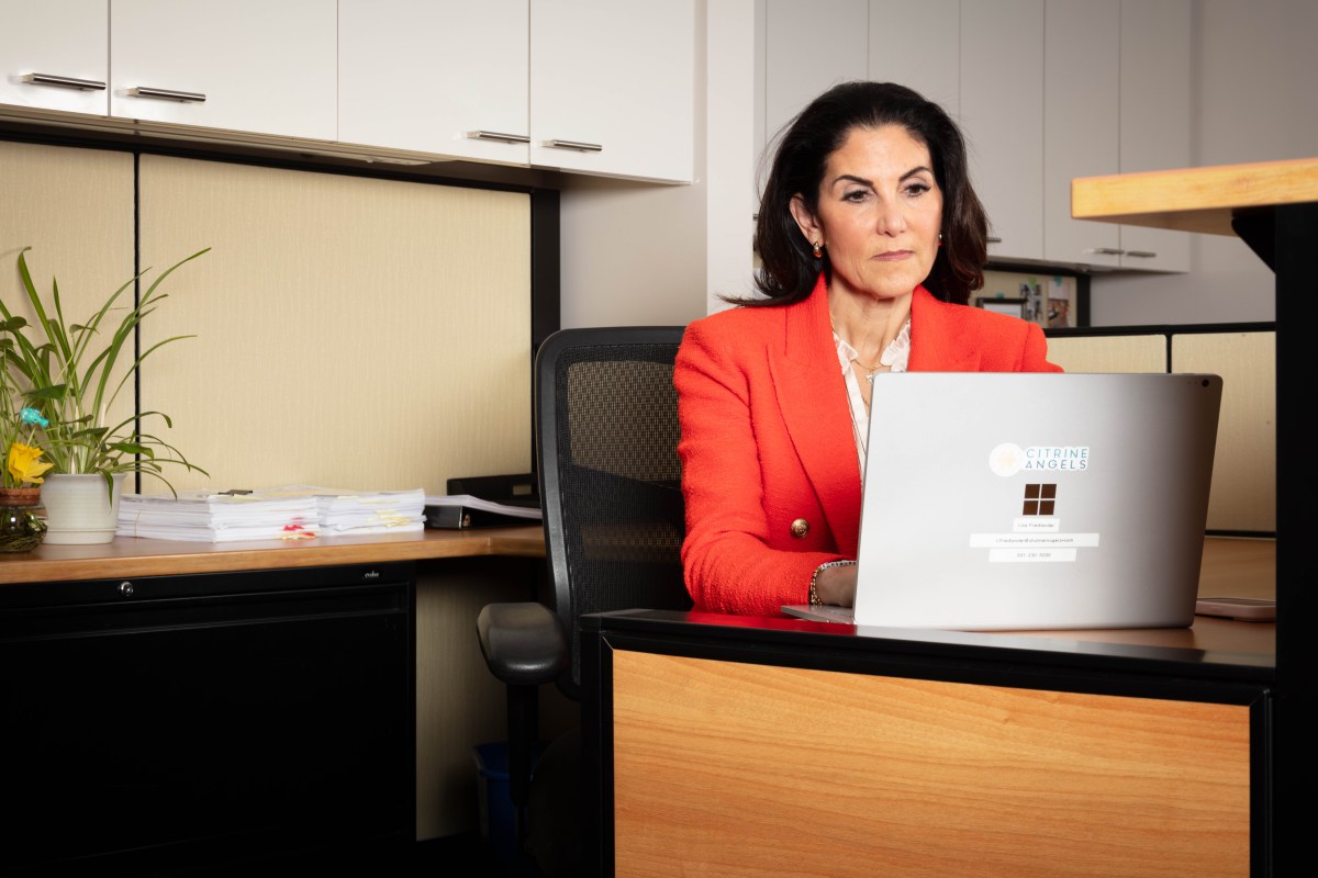 A woman in a red blazer sits at a desk with a laptop